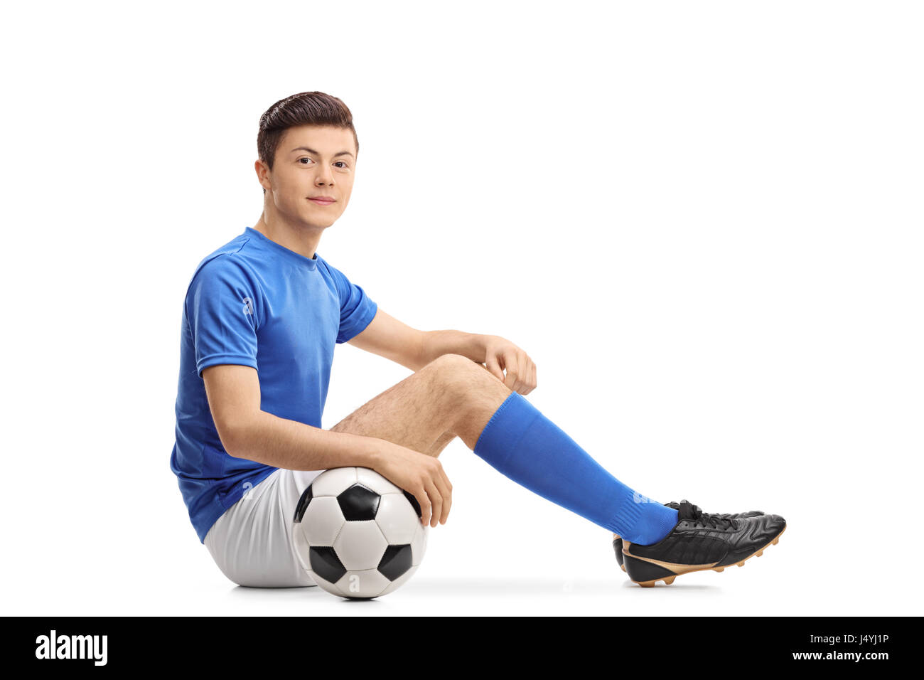 Calcio Teenage giocatore seduto sul pavimento e guardando la telecamera isolata su sfondo bianco Foto Stock