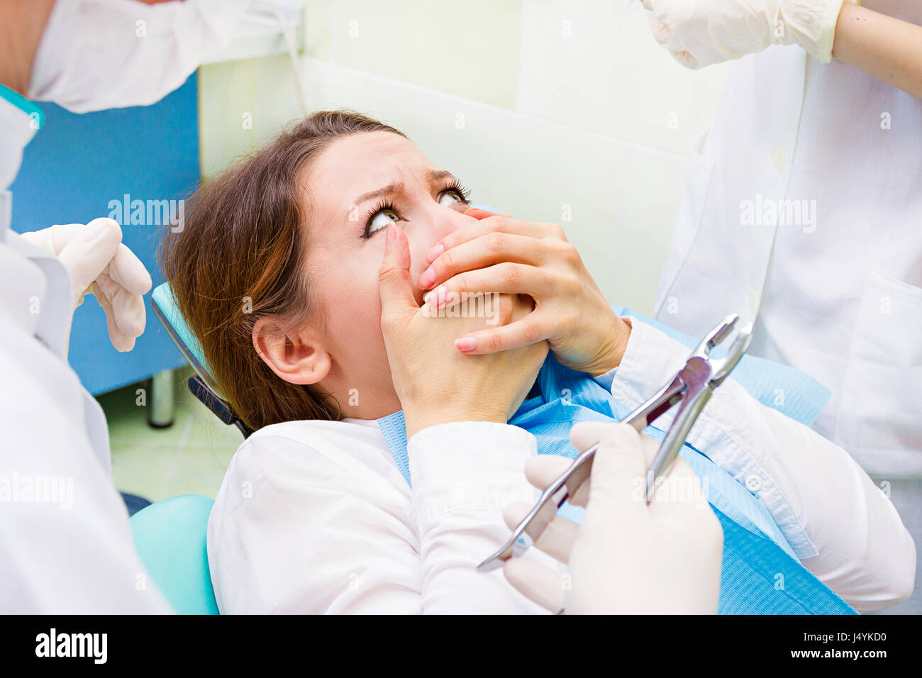 Closeup ritratto giovane ragazzina terrorizzata donna spaventata a visita dal dentista, ubicazione in cattedra, che copre la sua bocca non desidera procedura dentale, foratura, troppo Foto Stock