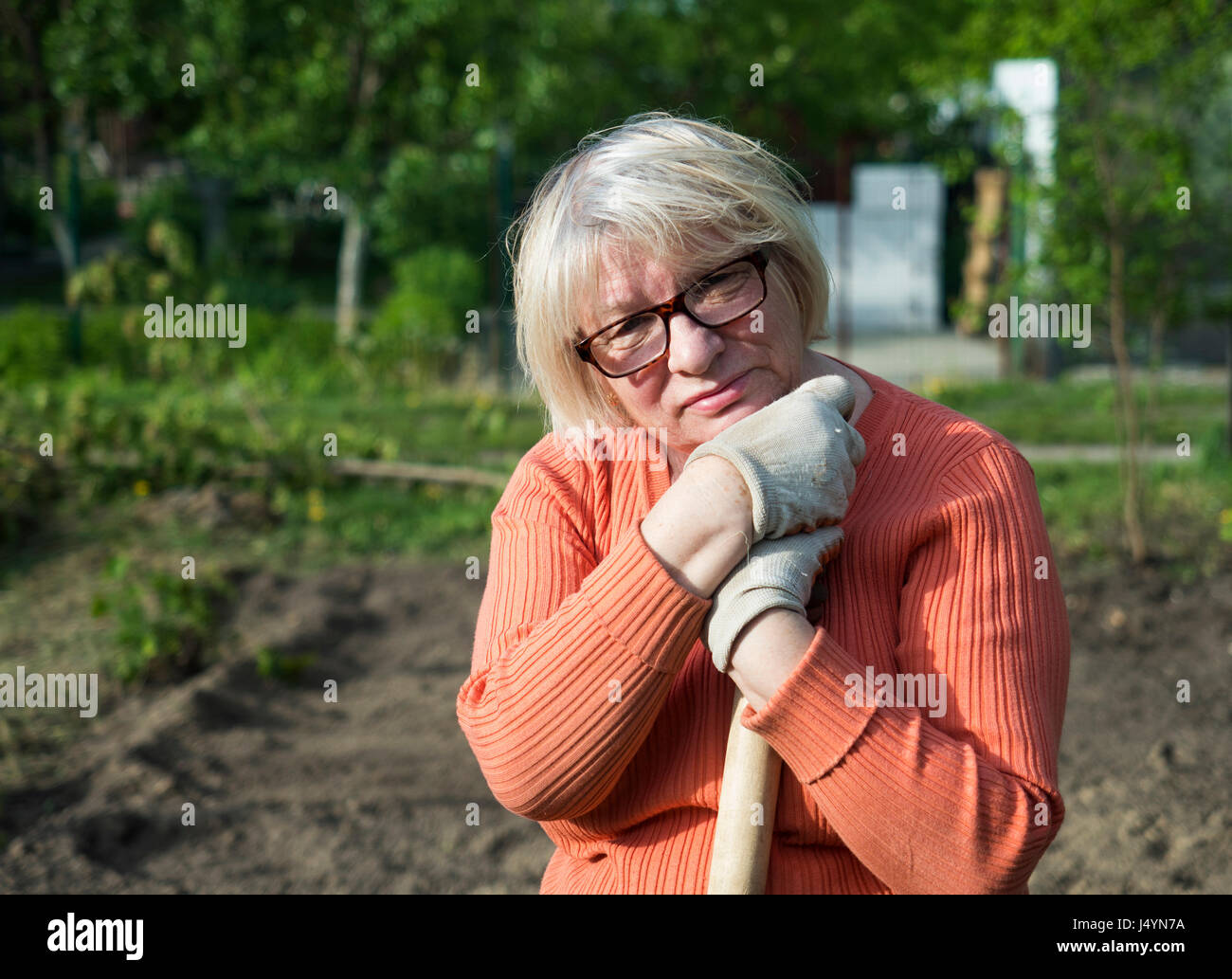 Caucasian donna di mezza età si appoggia sul manico della pala in giardino Foto Stock