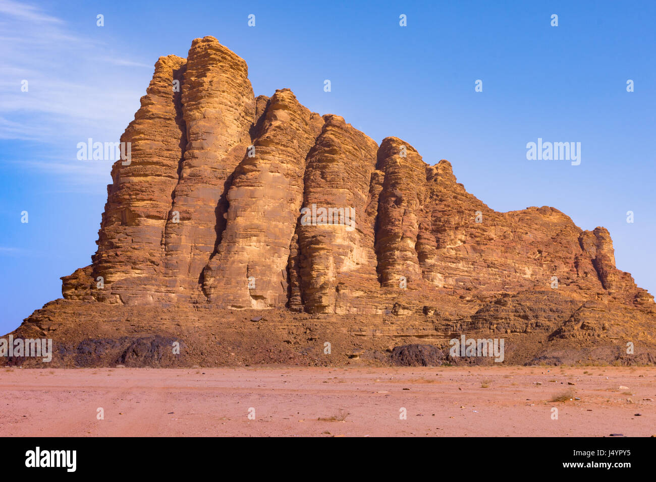 Sette Pilastri della saggezza, un robusto, Rocky Mountain nel Wadi Rum Desert, Giordania. Sabbia arancione è in primo piano e profondo cielo blu e nuvole sottili sopra Foto Stock