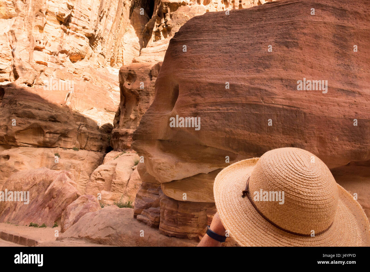 Donna che indossa un cappello di paglia, guardando le colorate in arenaria Al-Siq, Petra Giordania. La donna il cui hat corrisponde la pietra si trova in basso a destra. Foto Stock