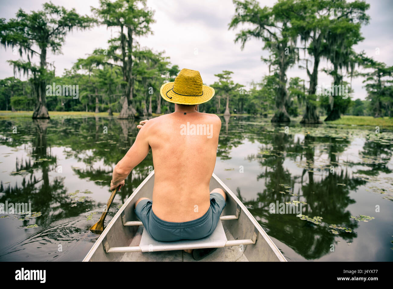 L'uomo con il cappello seduti nella parte anteriore di una canoa kayak in una palude scuro in scena a caddo Lake, Texas Foto Stock