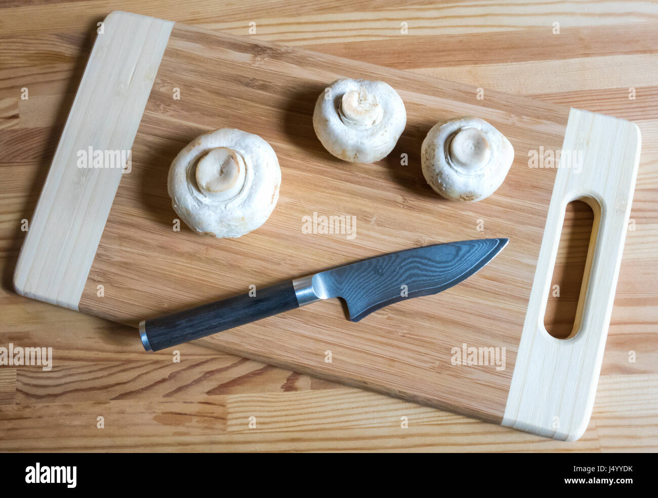 Tre grossi funghi a bottoni e un coltello da parare su un tagliere di legno Foto Stock