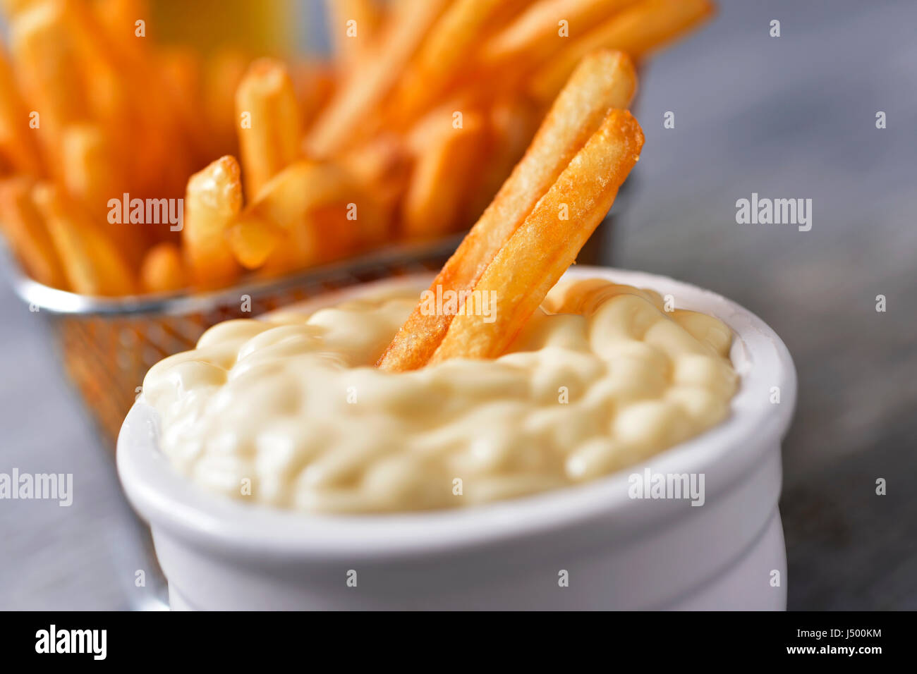 Primo piano di un bianco di ceramica ciotola con la maionese e alcuni appetitosi patatine fritte servite in un cestello di metallo, il grigio di una tavola in legno rustico Foto Stock