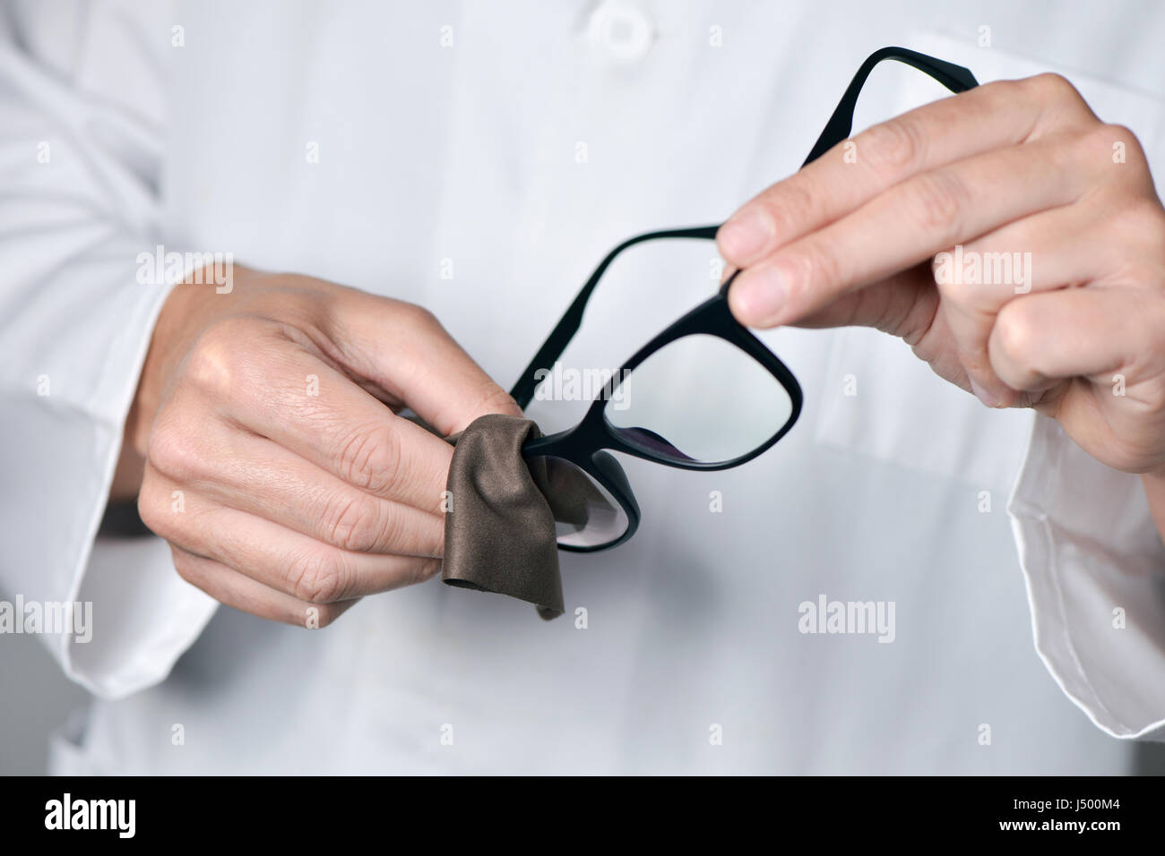 Primo piano di un giovane uomo ottico in un manto bianco pulizia delle lenti di un paio di occhiali con un panno in microfibra Foto Stock