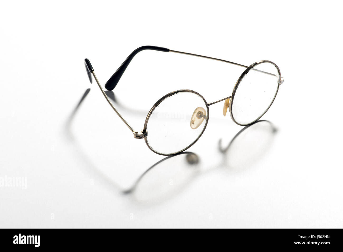 Coppia di classica rotonda occhiali vintage, un paio di occhiali o occhiali con un filo sottilissimo frame visualizzato aprire gettare un'ombra su un bianco riflettente backgrou Foto Stock