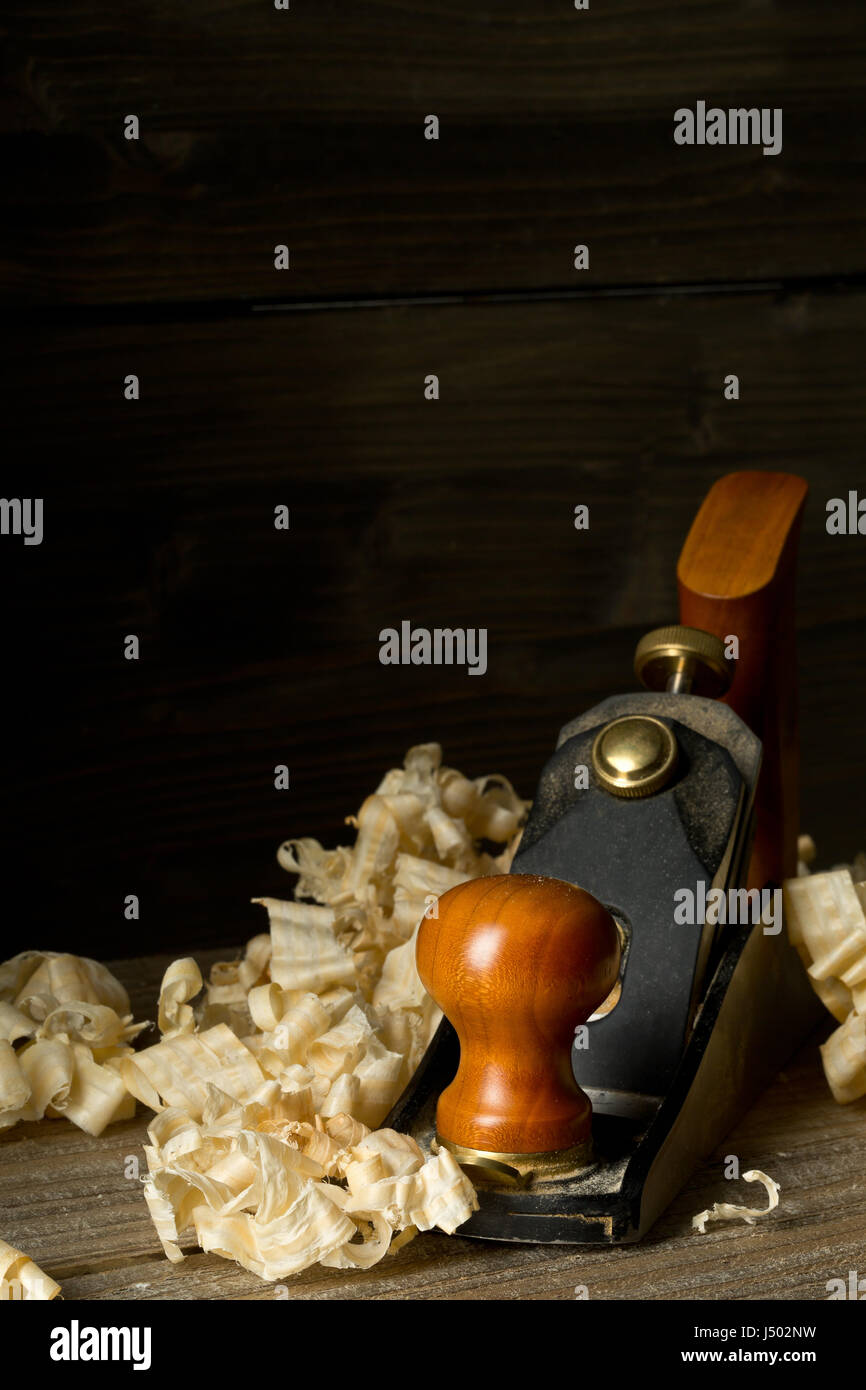 Macchine per la lavorazione del legno Pialla a mano attrezzo su assi di legno nella bottega del falegname contro il marrone scuro dello sfondo con spazio di copia Foto Stock