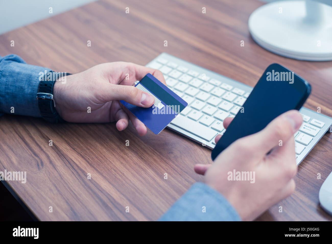 Mani tenendo la carta di credito e una digitazione sul telefono cellulare acquisto online Foto Stock