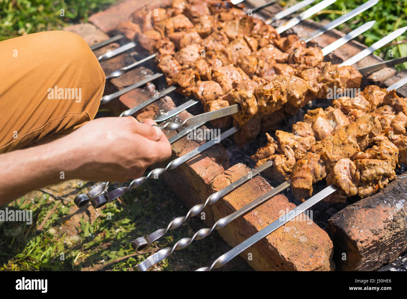 Mano d'uomo capovolgere kebab o il barbecue su una griglia di mattoni. Concetto di viaggio Foto Stock