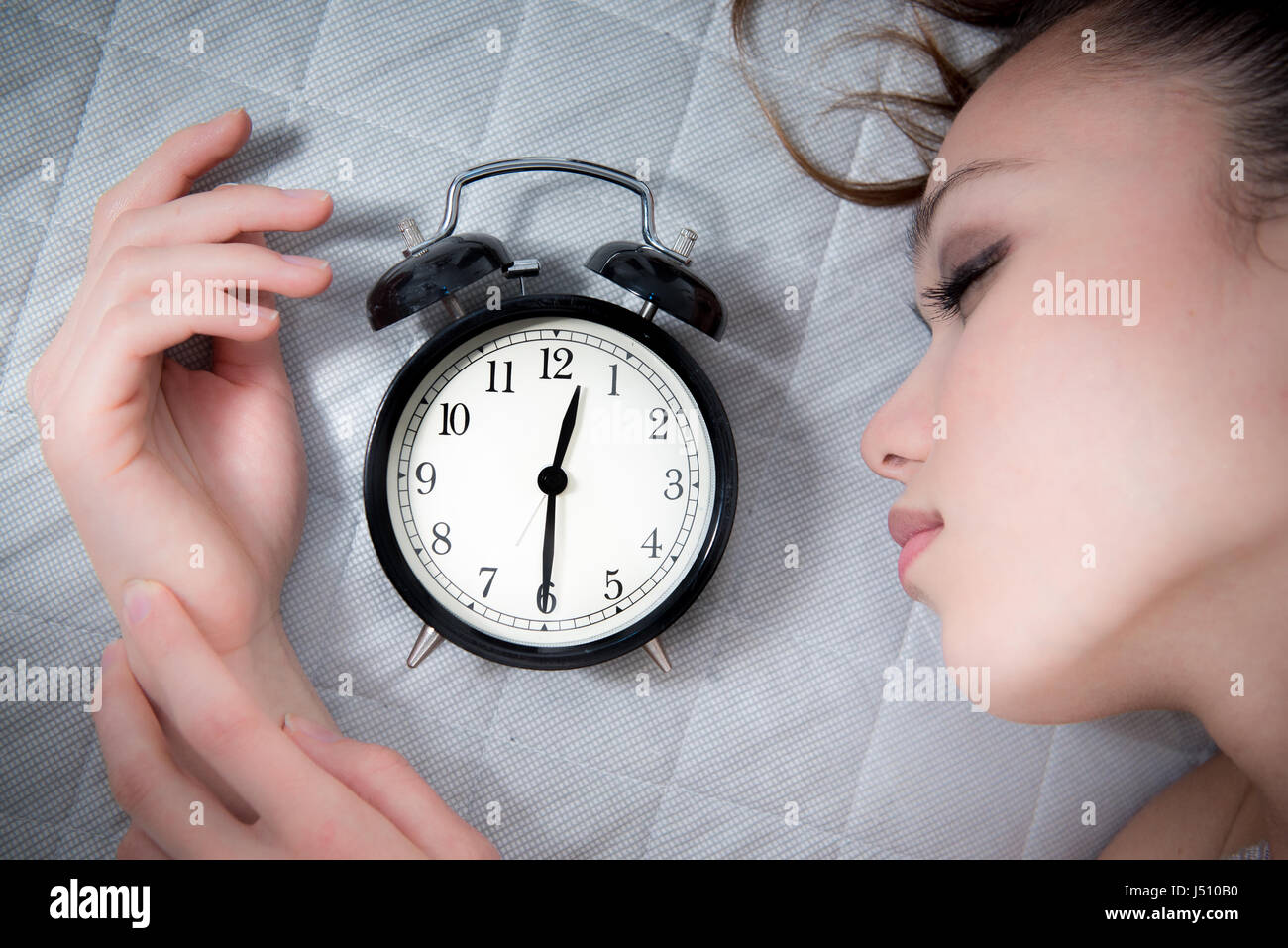 Bella donna headshoot, dormire con il nero orologio sveglia vicino al viso Foto Stock