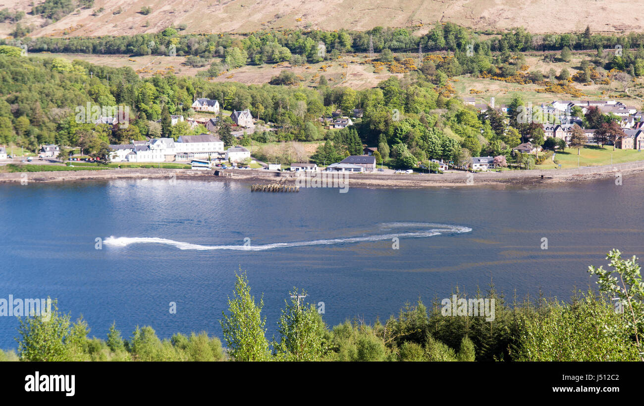 Una barca veloce rende onde in Loch Long, un mare loch in Occidente Highlands della Scozia, con Arrochar villaggio dietro. Foto Stock