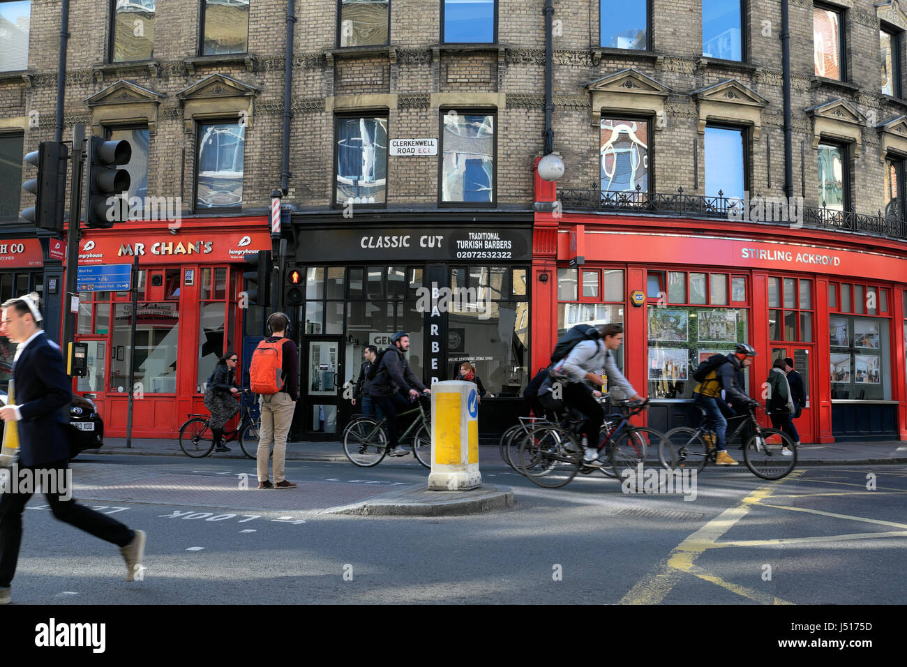 L'uomo della strada di attraversamento e persone in bicicletta al lavoro passato piccoli negozi all'angolo di St John Street e Clerkenwell Road a Londra CE1 UK KATHY DEWITT Foto Stock