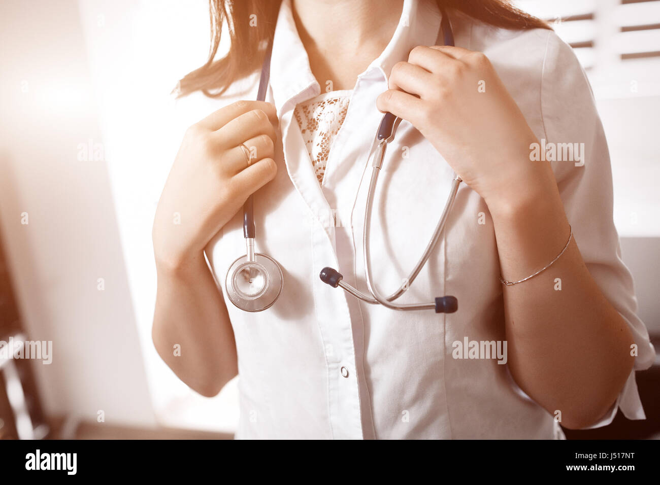 Un giovane medico donna in un bianco smock tenendo uno stetoscopio in bracci sul collo. Sfondo sfocato. Concetto di assistenza medica. Foto Stock