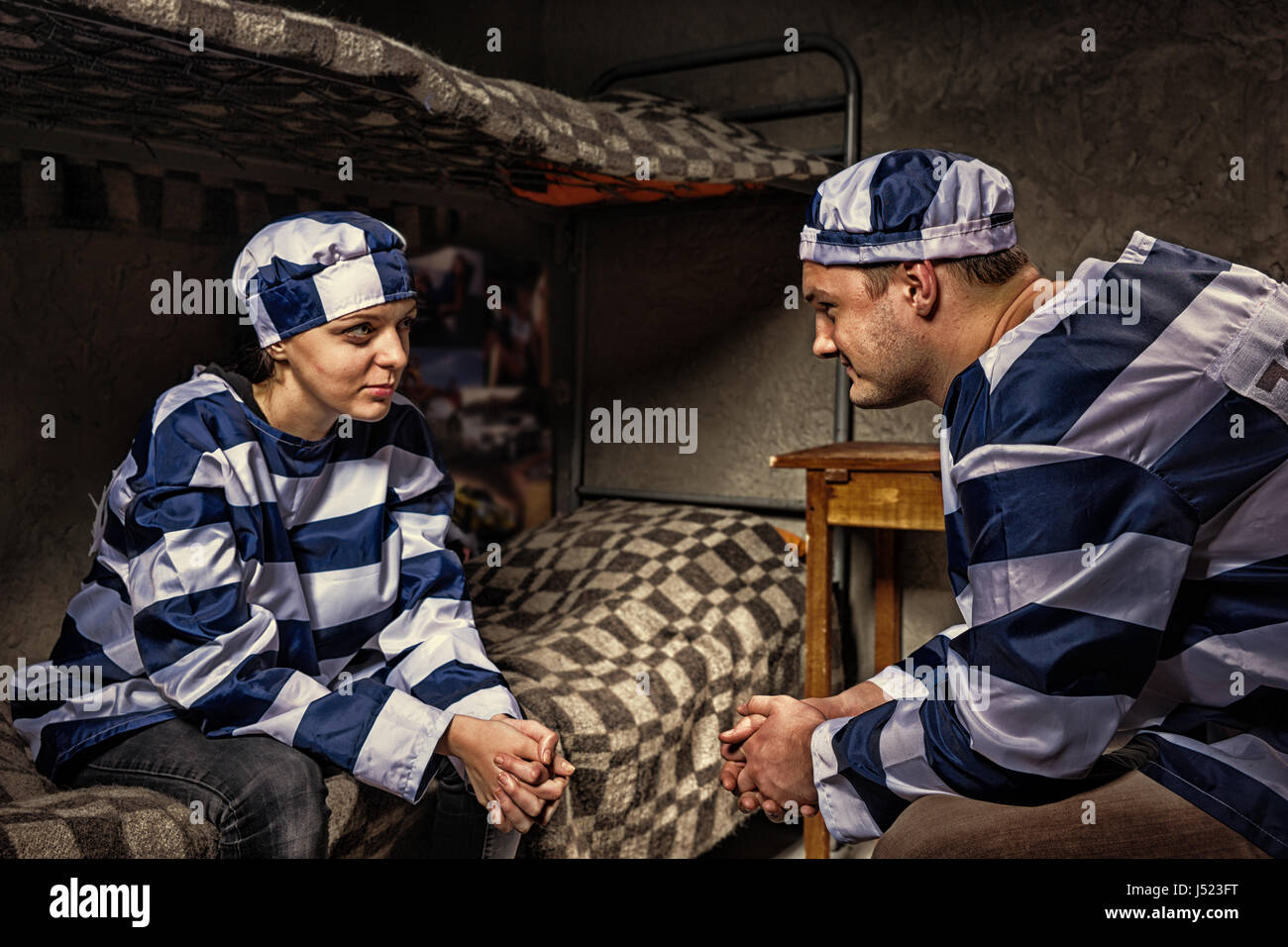 Maschio e femmina prigionieri indossano uniformi di prigione seduti vicino al comodino e guardando ogni altro in una cella di prigione Foto Stock