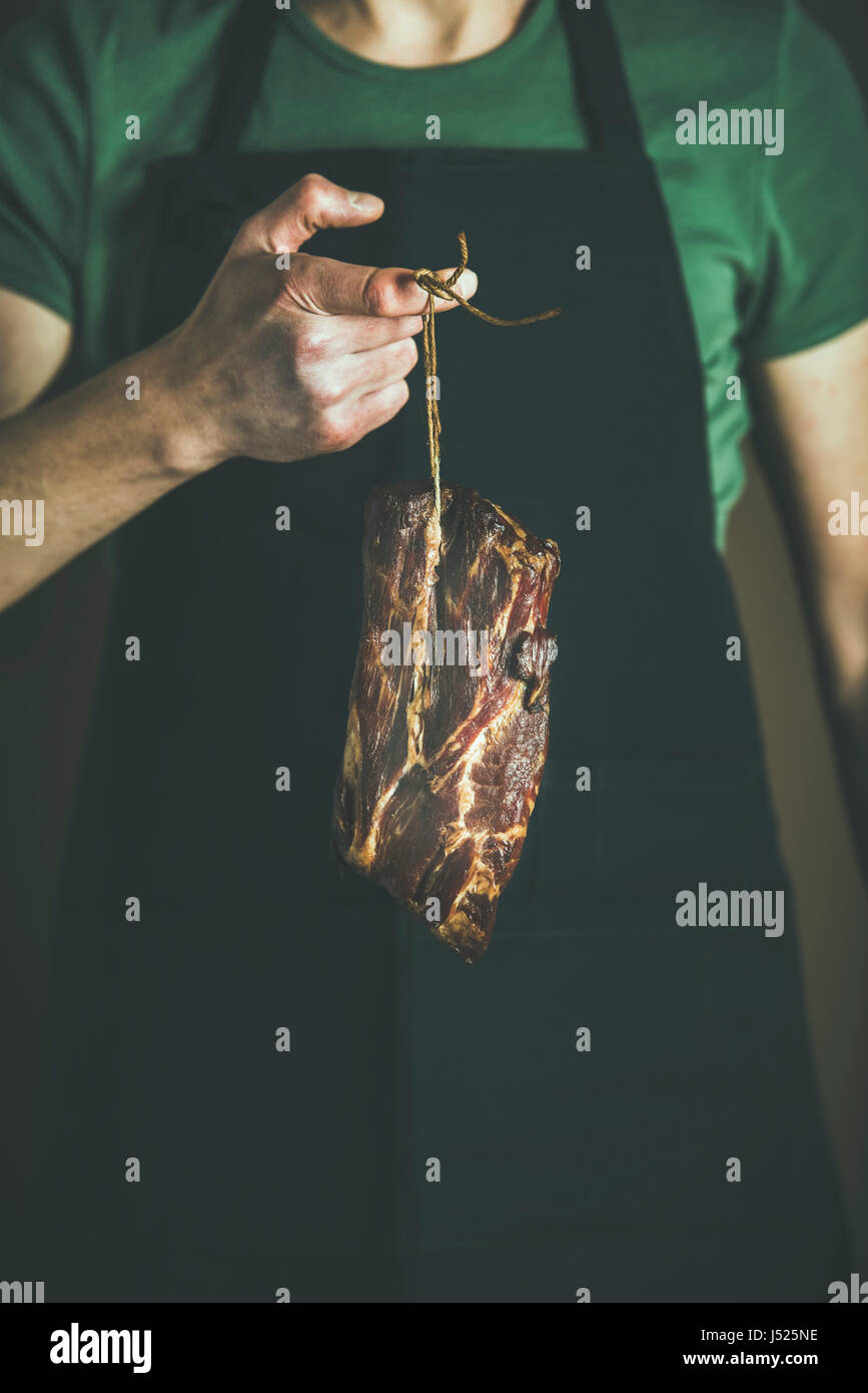 Uomo in nero grembiule mantenendo il taglio di insaccati in mano a livello locale mercato degli agricoltori. Gourmet, cibo organico concetto Foto Stock