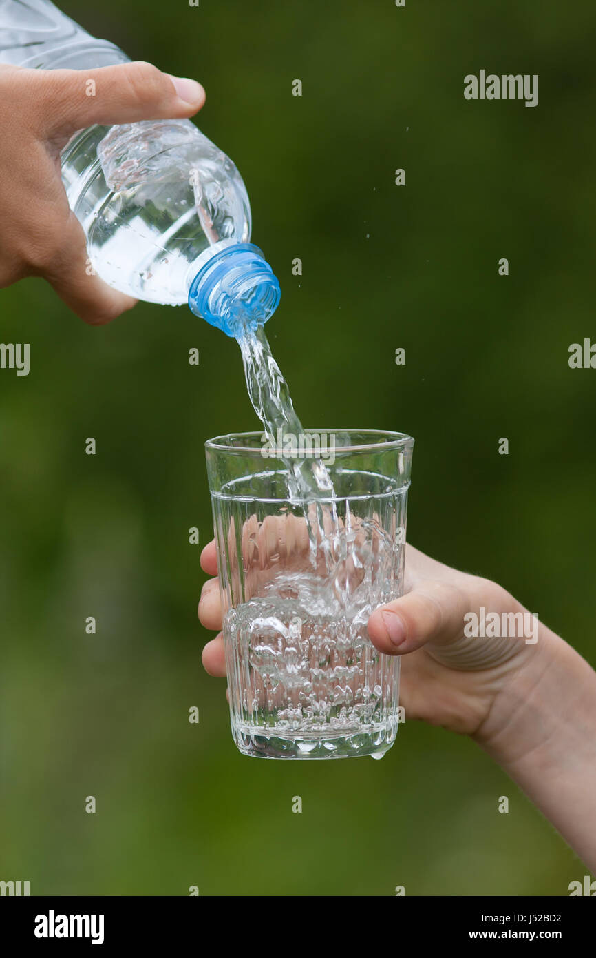 La mano di un adulto versando acqua pulita dal flacone in vetro del bambino sul verde sfondo sfocato Foto Stock