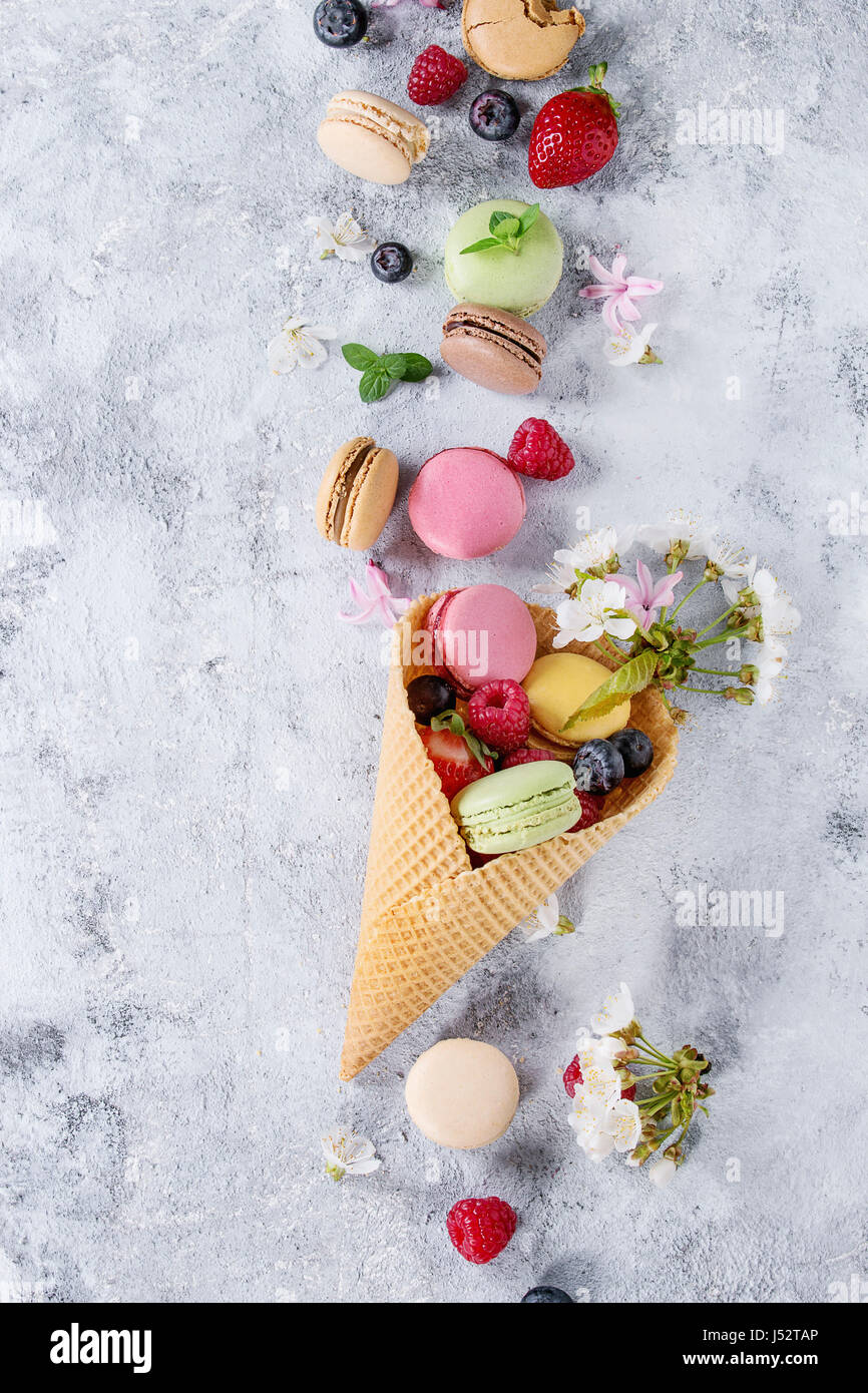 Varietà di coloratissimi francese dessert dolci macarons con vari ripieni serviti nel cono di cialda con menta e frutti di bosco freschi su grigio backgrou texture Foto Stock
