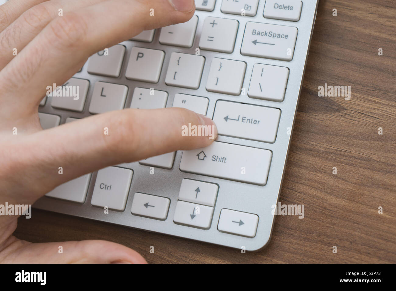 Mano d'uomo premendo il tasto di invio sulla tastiera wireless sul tavolo di legno Foto Stock