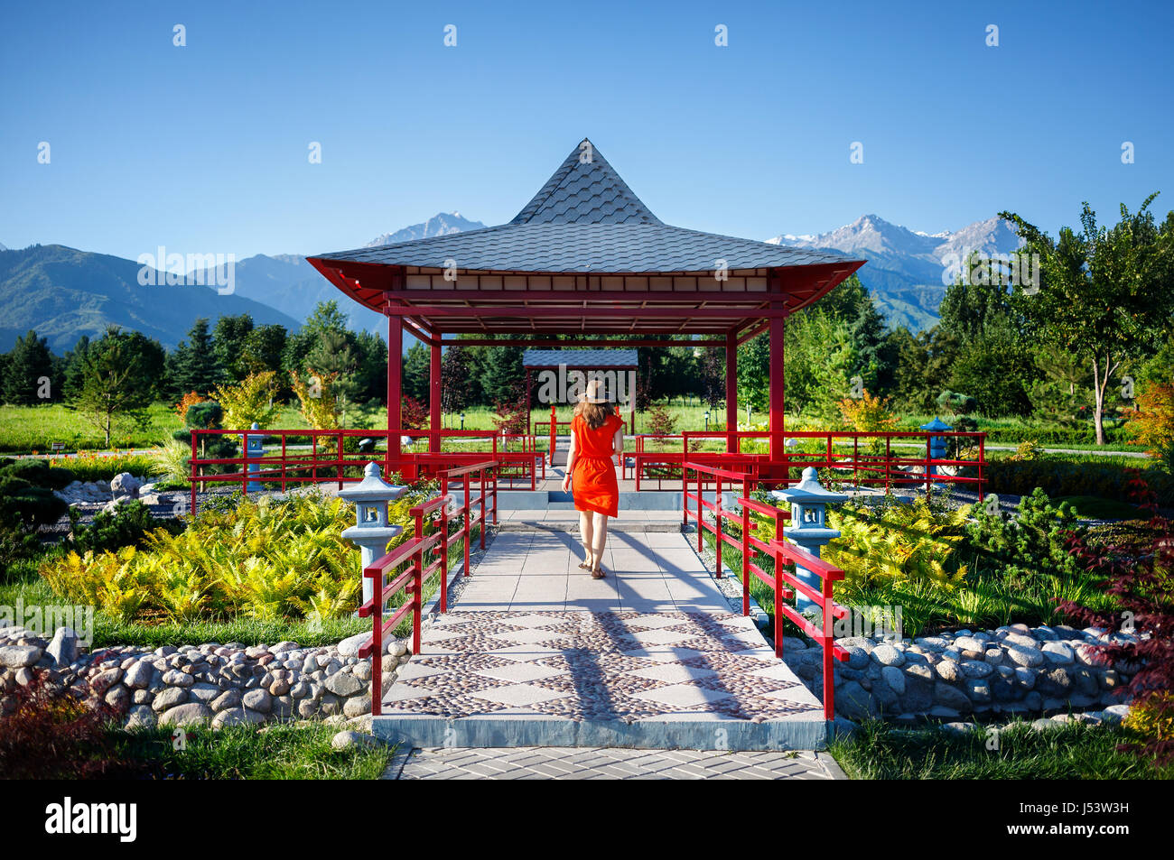 Donna in abito arancione con hat andando alla Pagoda giapponese giardino Foto Stock