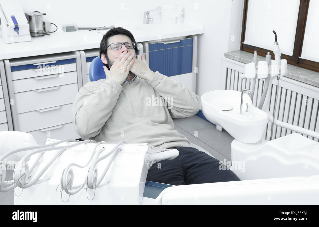 Molto terrorizzato adulto uomo seduto in poltrona del dentista in chirurgia dentale Foto Stock