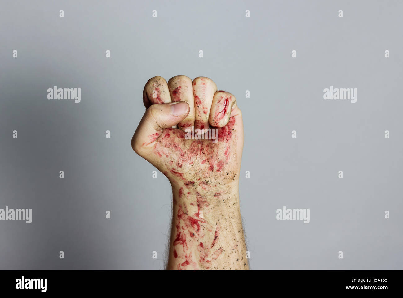 Sanguinosi e sporco pugno sinistro sollevando davanti a uno sfondo grigio Foto Stock
