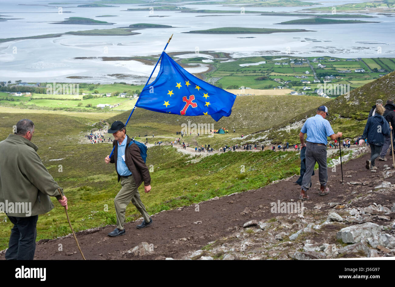 Uomo con Euro bandiera cristiana ascendente Croagh Patrick su 'Reek domenica" Foto Stock