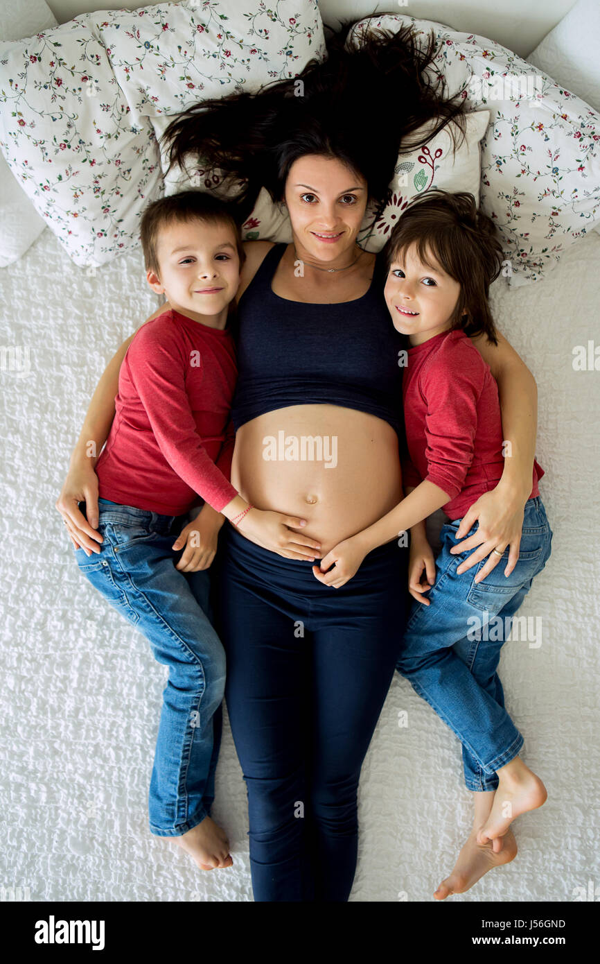 Bella incinta giovane madre e i suoi due bambini, ragazzi, giacenti nel letto di casa Foto Stock