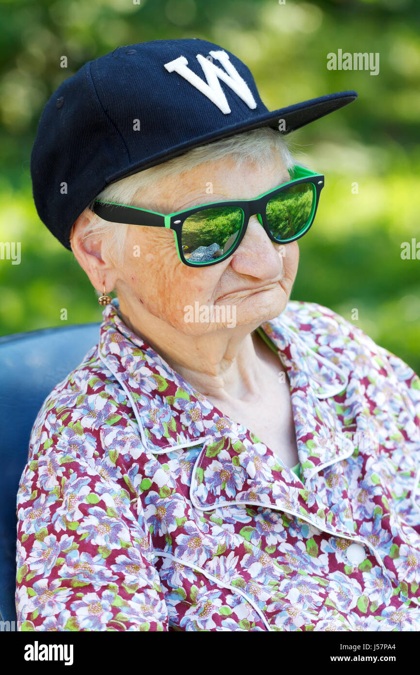 Senior donna che indossa gli occhiali da sole e cappello da baseball Foto Stock