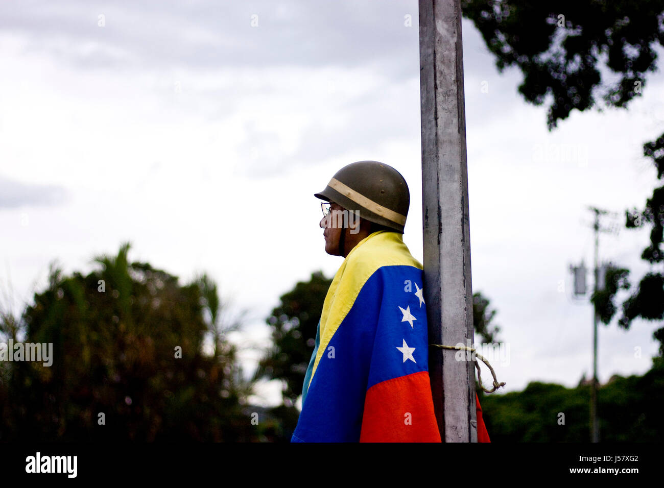 Un manifestante utilizzando un elmetto militare e la bandiera del Venezuela. Foto Stock