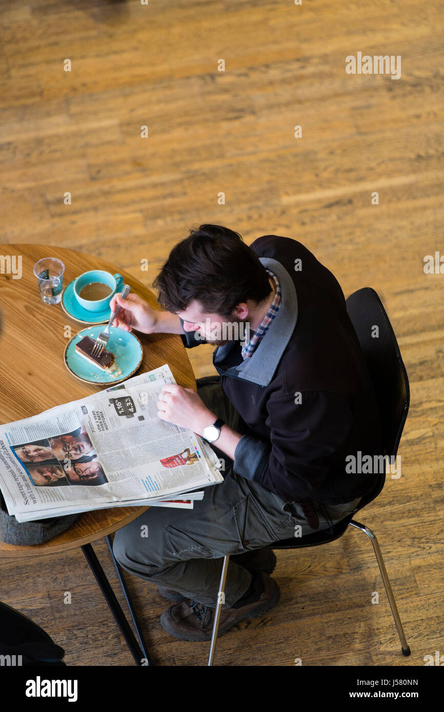 Media tradizionali NEL REGNO UNITO: una vista aerea di un uomo di bere il caffè , mangiare la torta e la lettura del Guardian - un broadsheet quotidiano britannico - in un Cafe Foto Stock