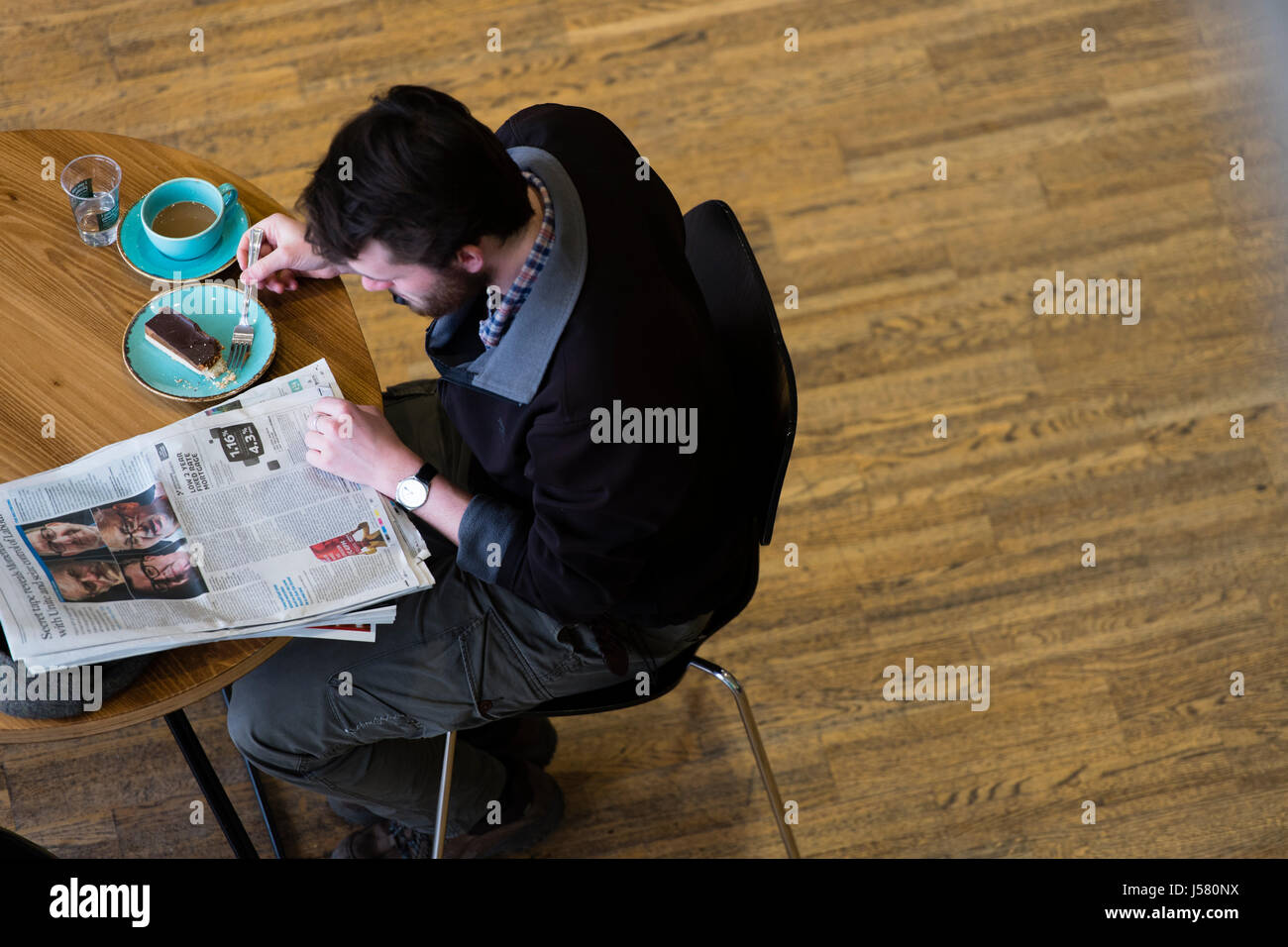 Media tradizionali NEL REGNO UNITO: una vista aerea di un uomo di bere il caffè , mangiare la torta e la lettura del Guardian - un broadsheet quotidiano britannico - in un Cafe Foto Stock