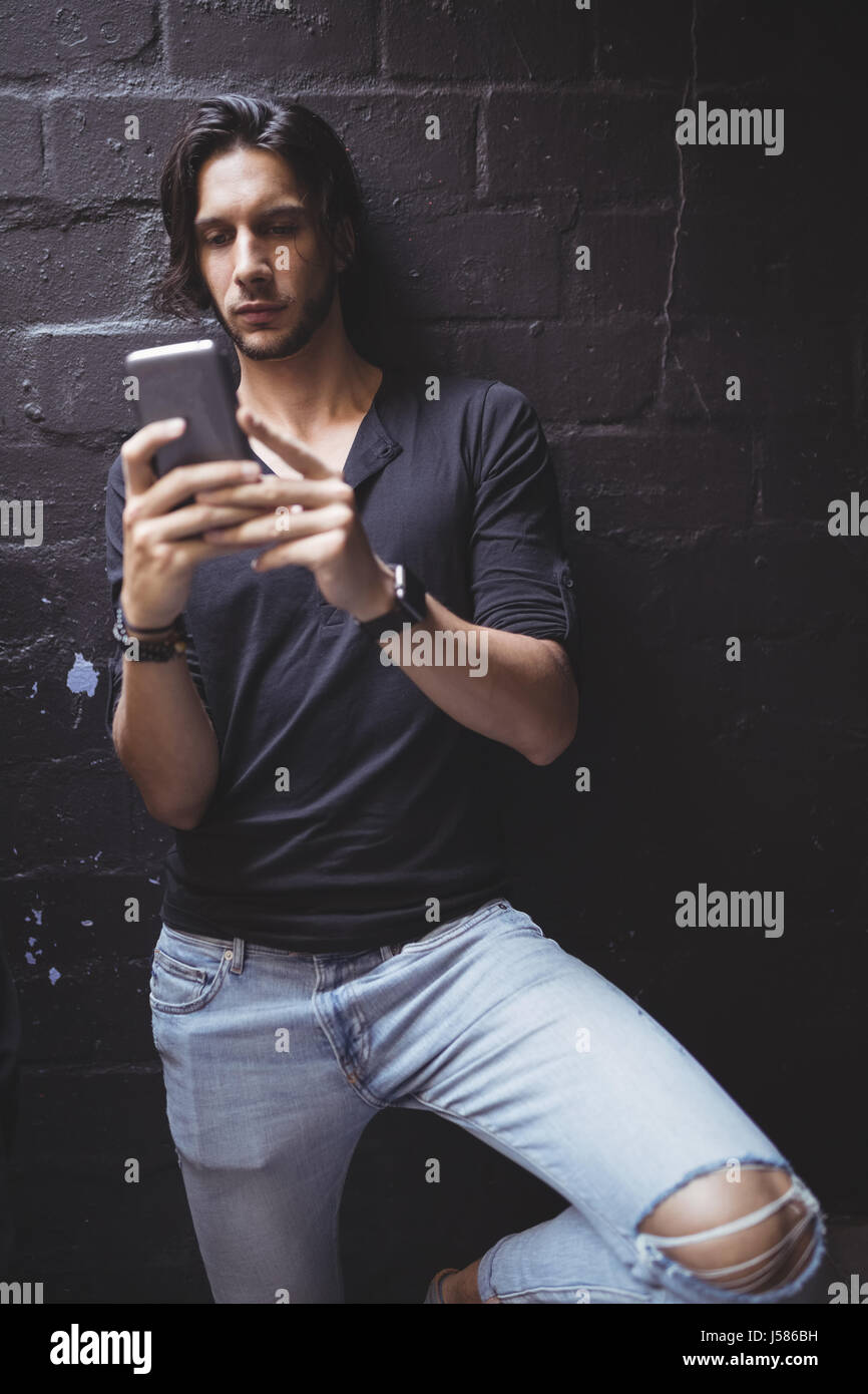 Giovane uomo Portare jeans strappati mentre si utilizza il telefono  cellulare contro il muro nero in discoteca Foto stock - Alamy