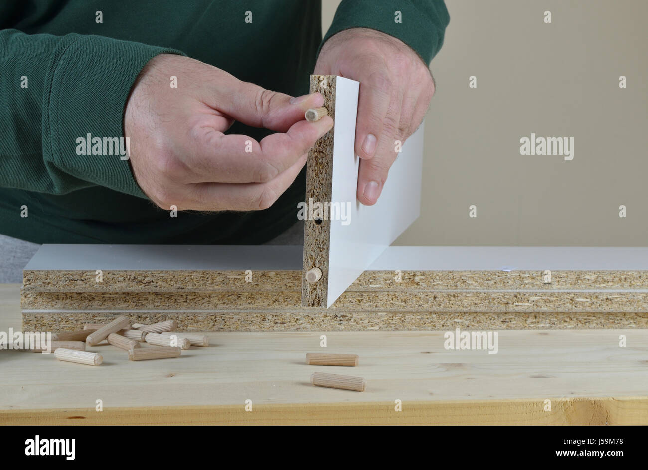 L'uomo l'inserimento di spine in legno in un pannello di particelle di un nuovo pezzo di arredamento Foto Stock