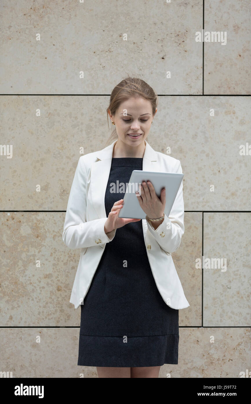 Caucasian Business donna tramite digital computer tavoletta appoggiata contro una parete di marmo. Foto Stock