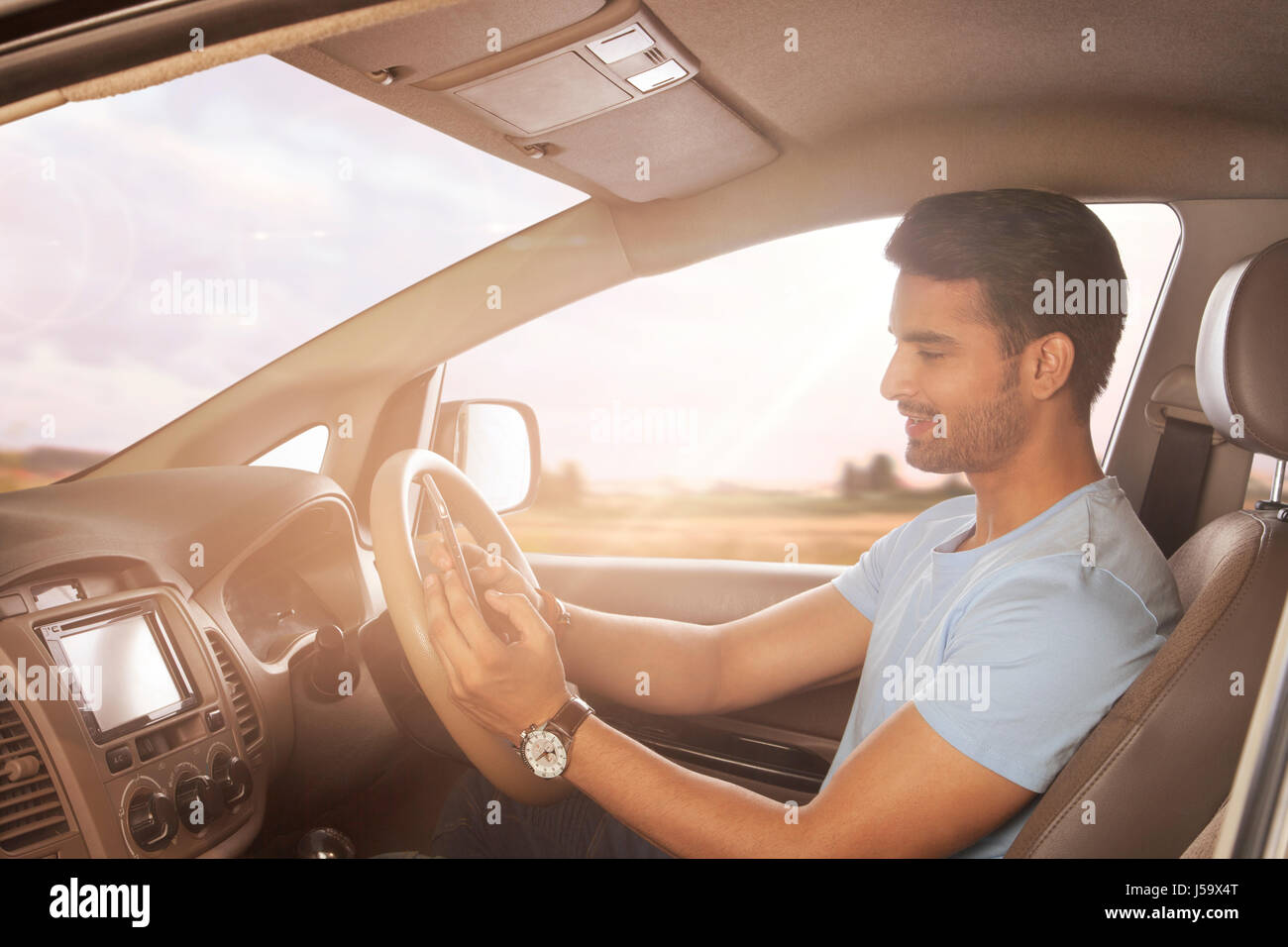 Giovane uomo utilizzando smart phone mentre si guida auto Foto Stock