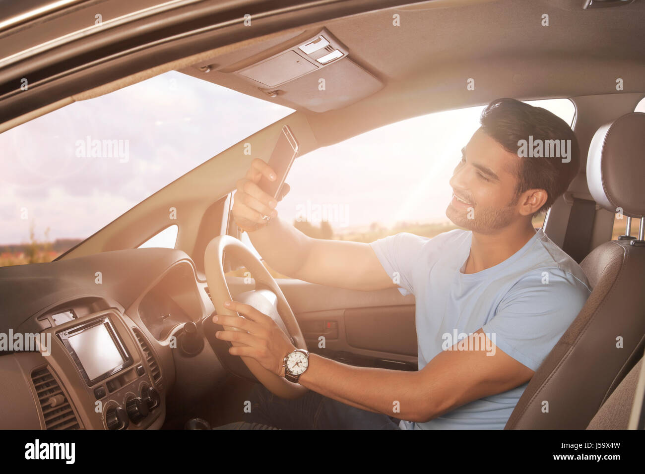 Sorridente giovane uomo utilizzando smart phone mentre si guida auto Foto Stock