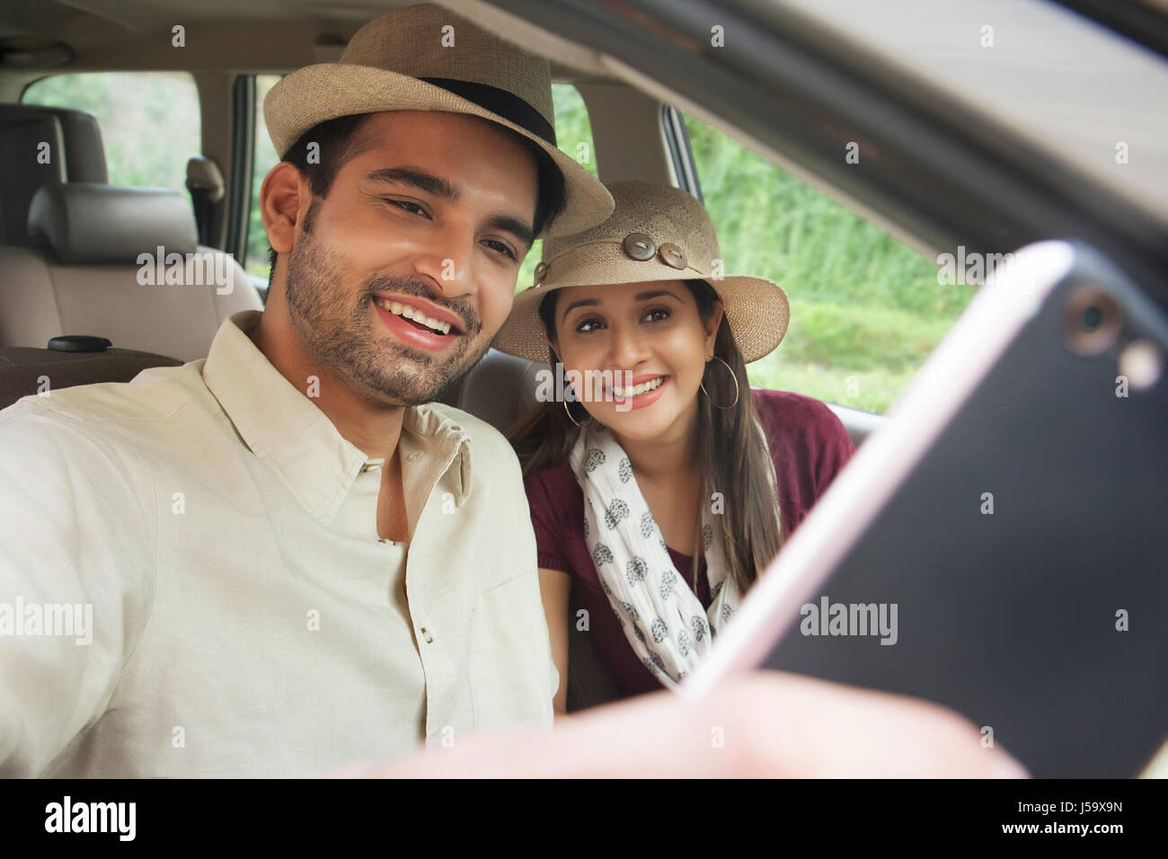 Coppia sorridente indossando hat prendendo un selfie in auto Foto Stock