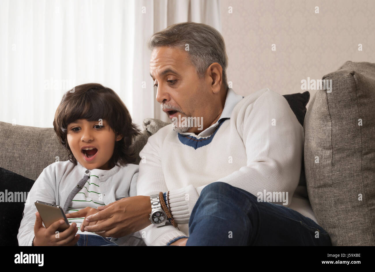 Felice nonno e nipote tramite telefono cellulare seduti insieme sul divano Foto Stock