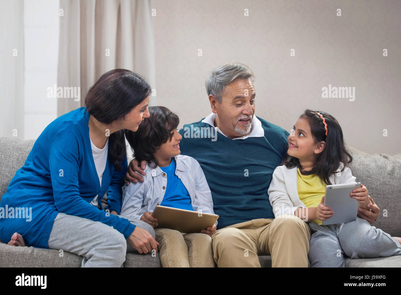 Felice nipoti con tavoletta digitale con i nonni seduti sul divano Foto Stock