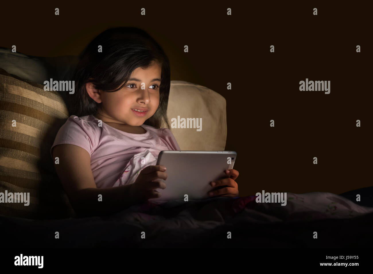 Bambina con tavoletta digitale nel letto di notte Foto Stock