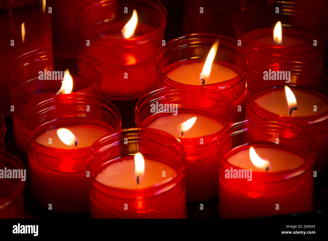 Grande gruppo di candele rosse che brillano nel buio Foto Stock