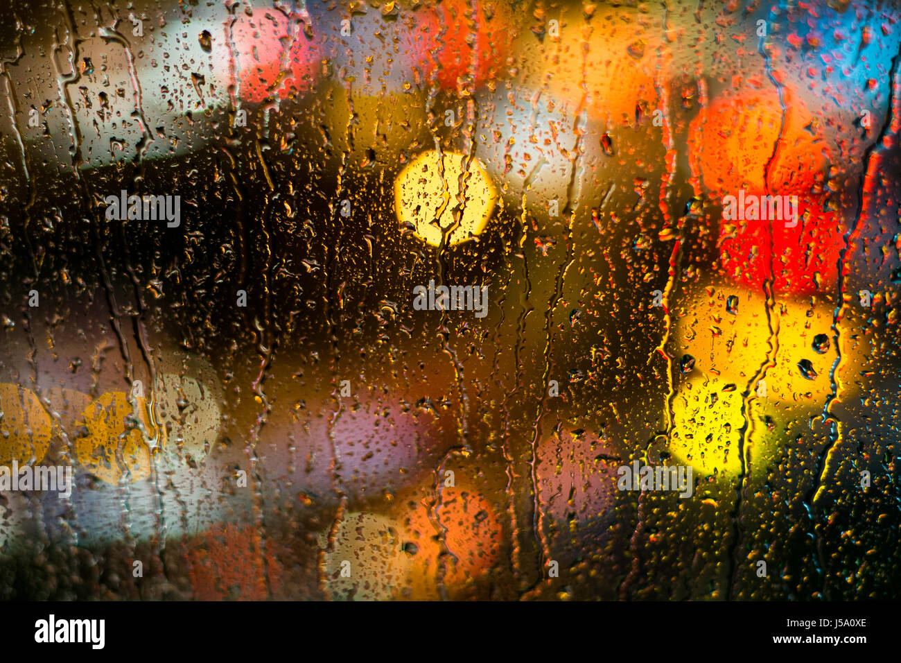 Auto sfocati luce dietro le gocce di pioggia Foto Stock