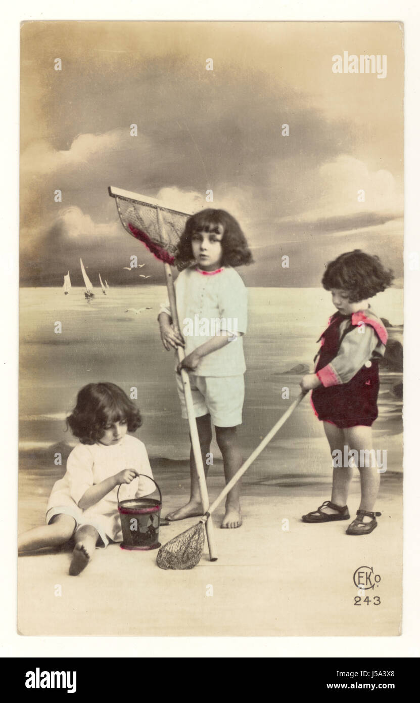 Ai primi del novecento ed oscurata cartolina francese di adorabili bambini con reti da pesca con una spiaggia sfondo impostato in uno studio fotografico, circa 1910, Francia Foto Stock