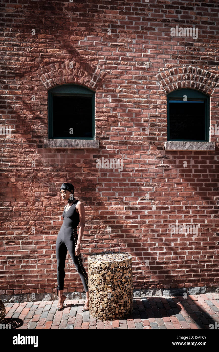 Adolescente femminile con pelle scura, ragazza adolescente, 20s, modello wannabe, aspirante, Posando da un muro di mattoni, il Distillery Historic District, Toronto, Ontario Foto Stock