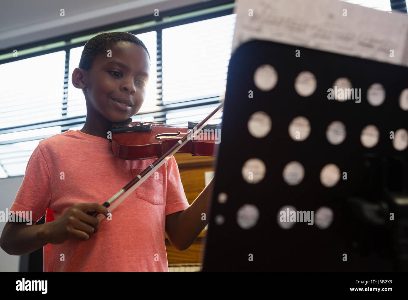 Ragazzo sorridente suona il violino mentre in piedi in aula a scuola Foto Stock