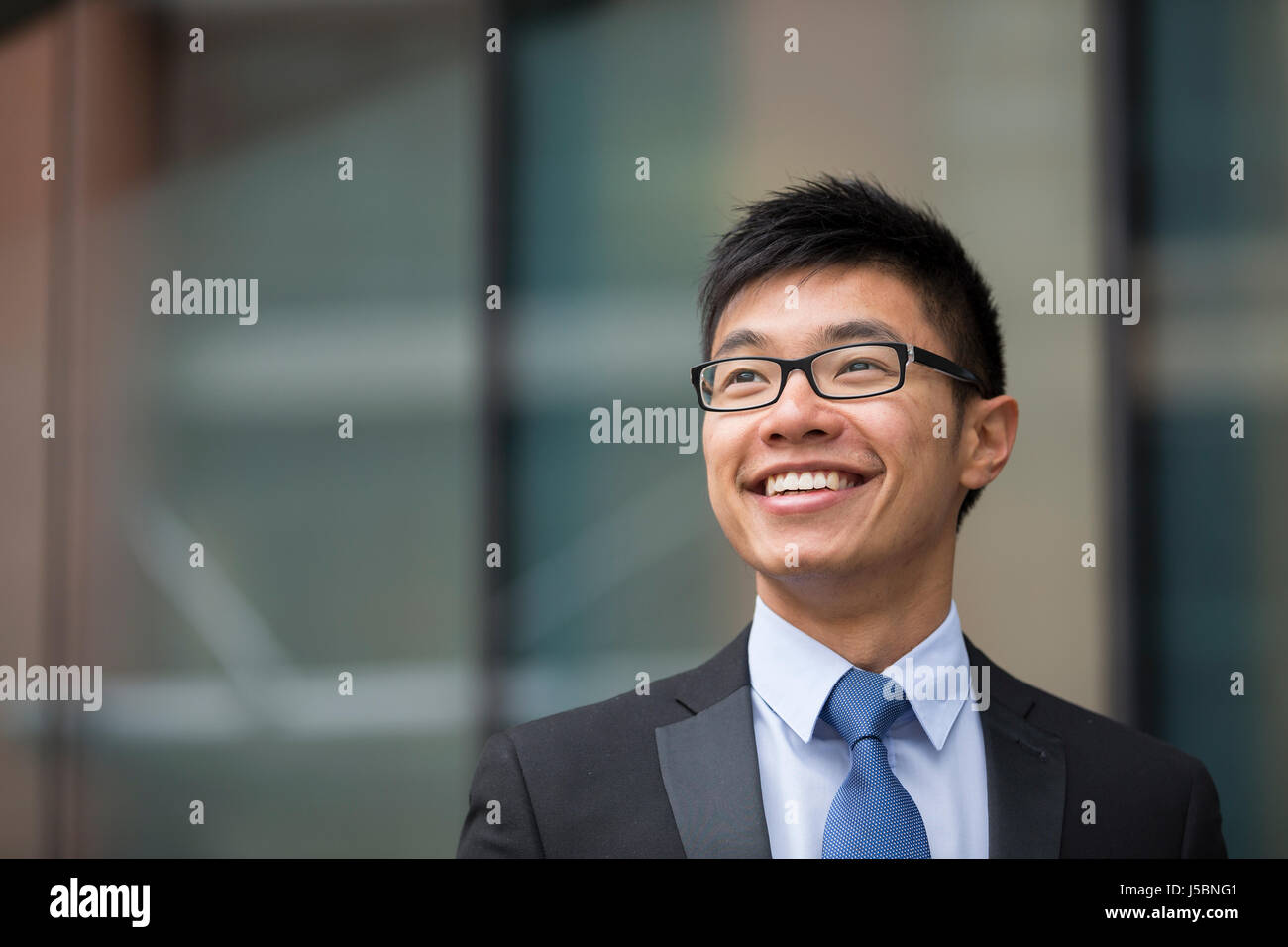 Ritratto di un imprenditore cinese al di fuori ufficio moderno edificio, guardando lontano. Foto Stock