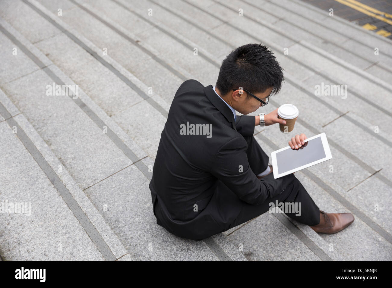 Elevato angolo di visione di un uomo cinese seduto su passaggi utilizzando un dispositivo tablet pc all'esterno. Foto Stock