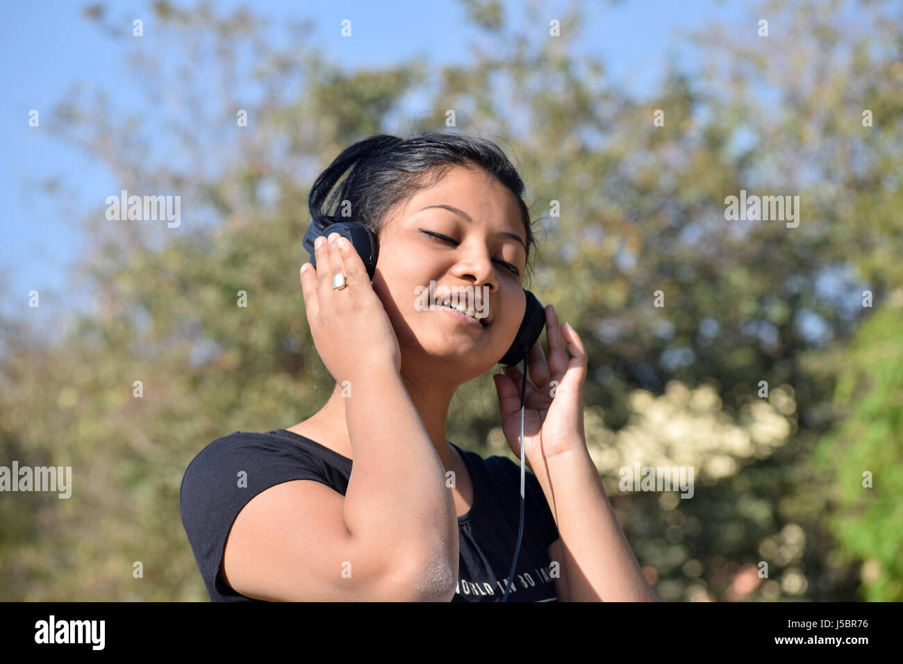 Ragazza giovane ascoltando musica in cuffia al di fuori nel giardino di Pune, Maharashtra Foto Stock