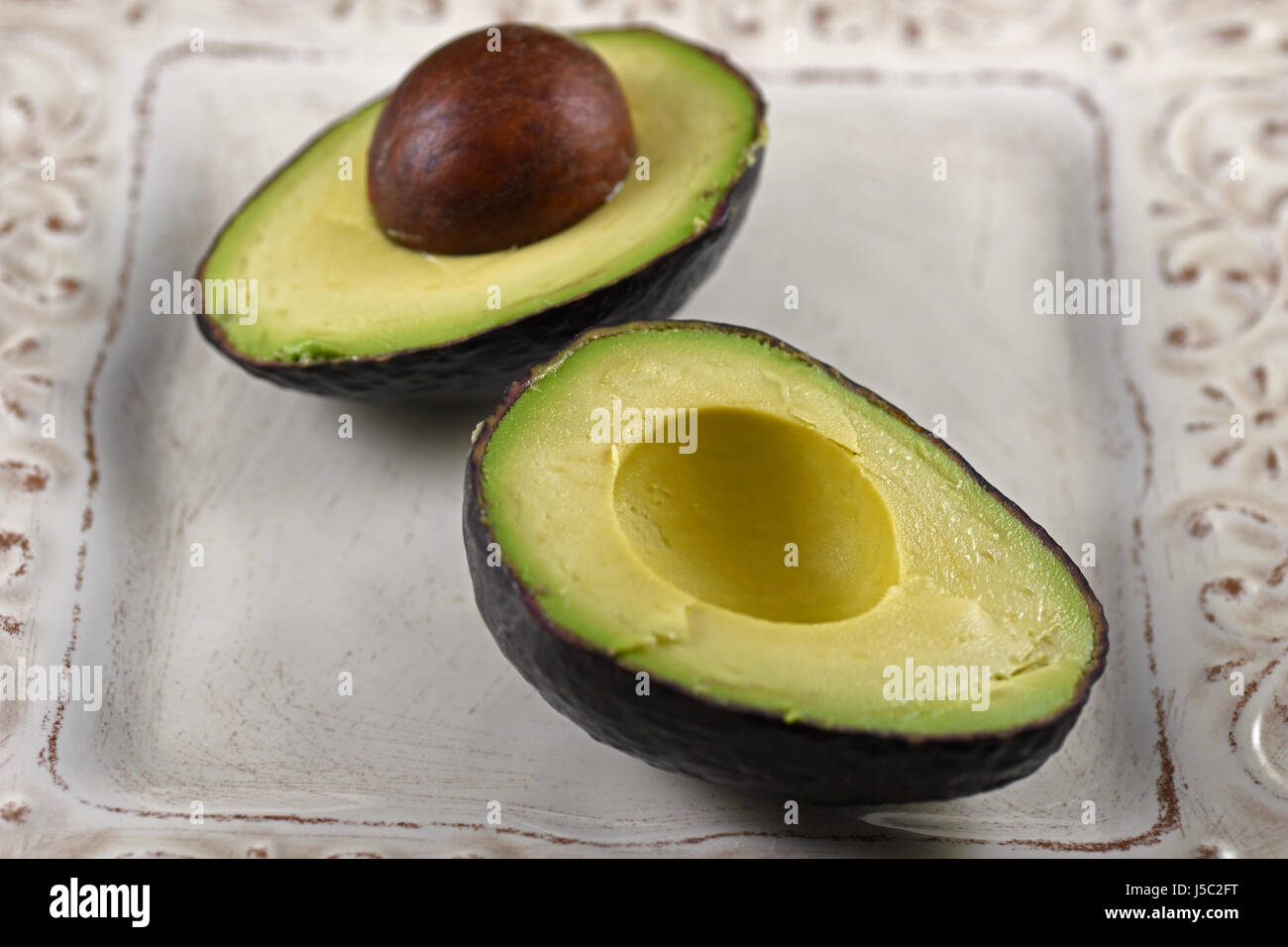 Raw metà di avocado su un piatto bianco Foto Stock