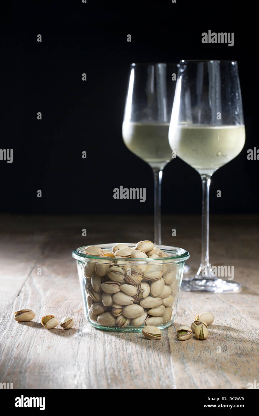 Ciotola di pistacchi e due bicchieri di vino bianco seduto su una tavola in legno rustico. Foto Stock
